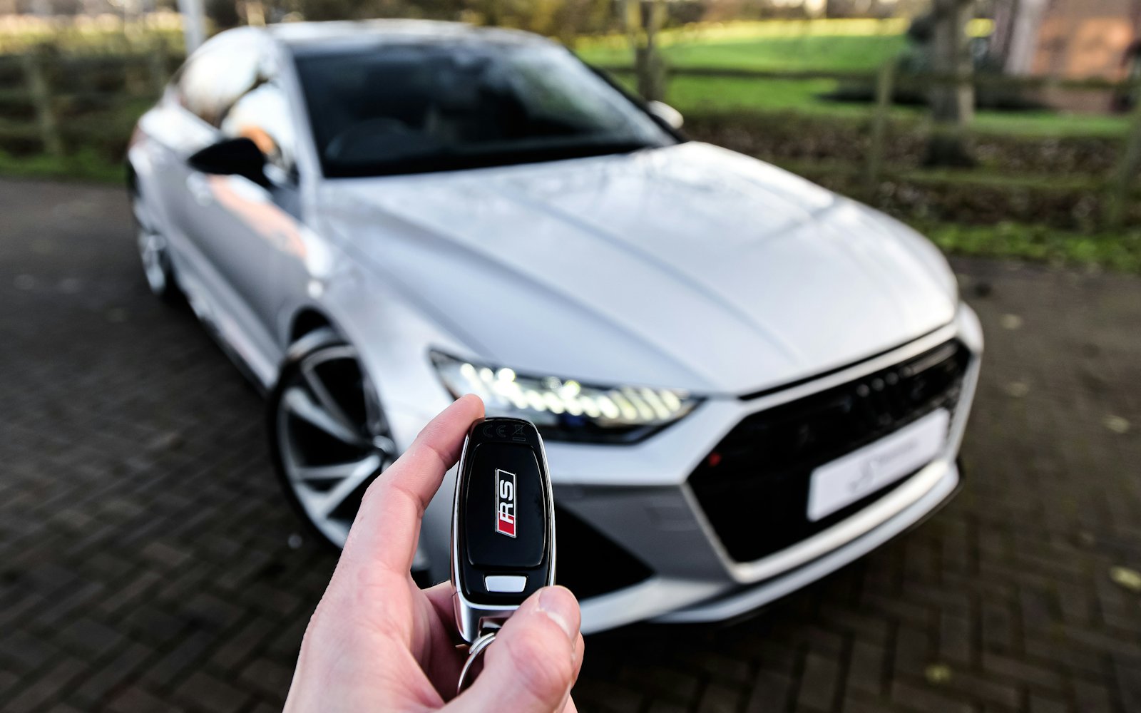 Hand mit Autoschlüssel vor einem silbernen Fahrzeug